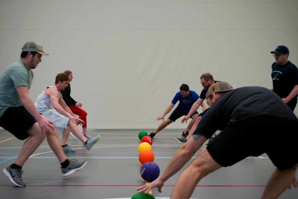 People in a gym reaching for colorful balls during a game.