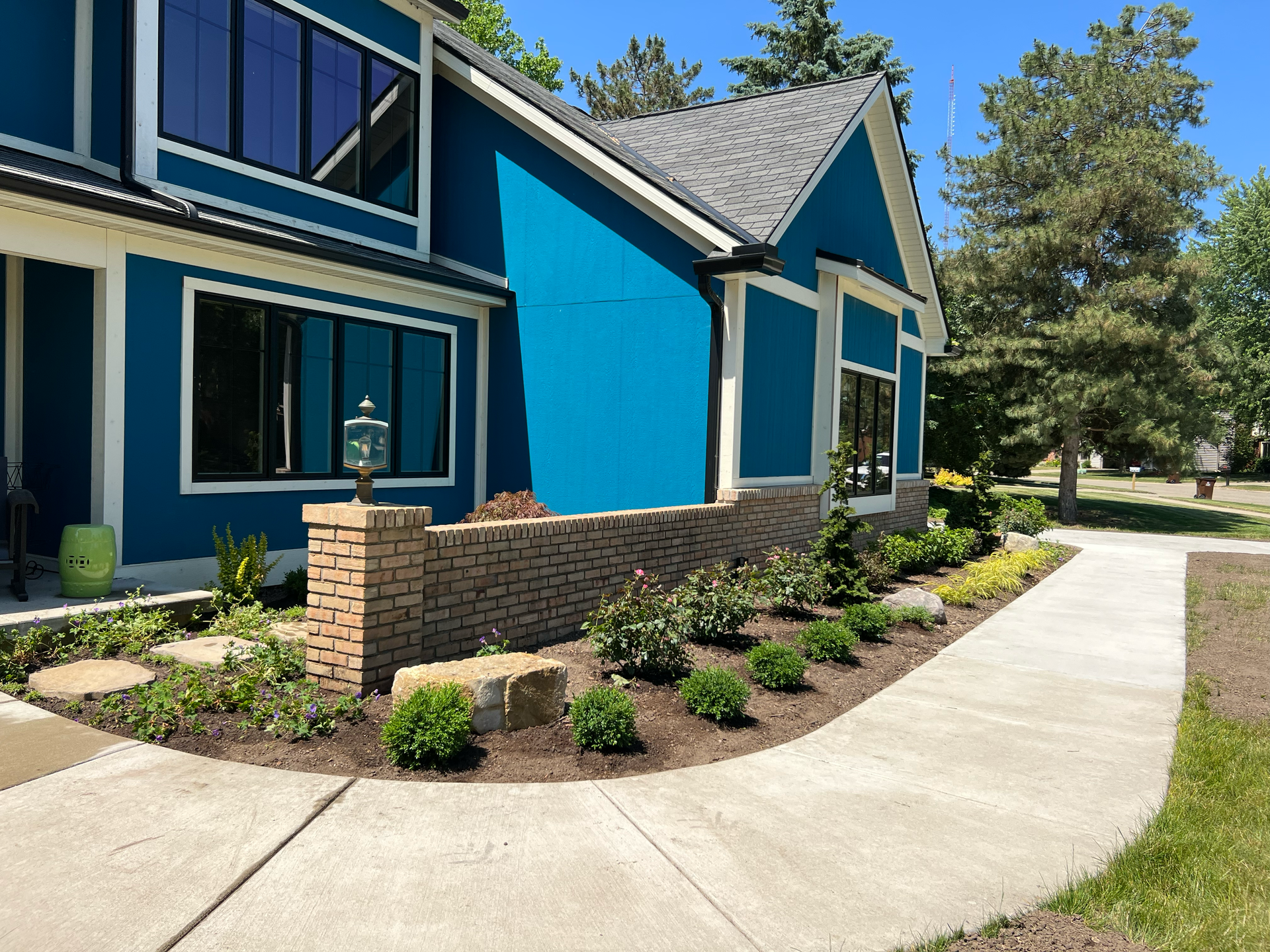 Blue house with landscaping, brick wall, and a curved sidewalk on a sunny day.
