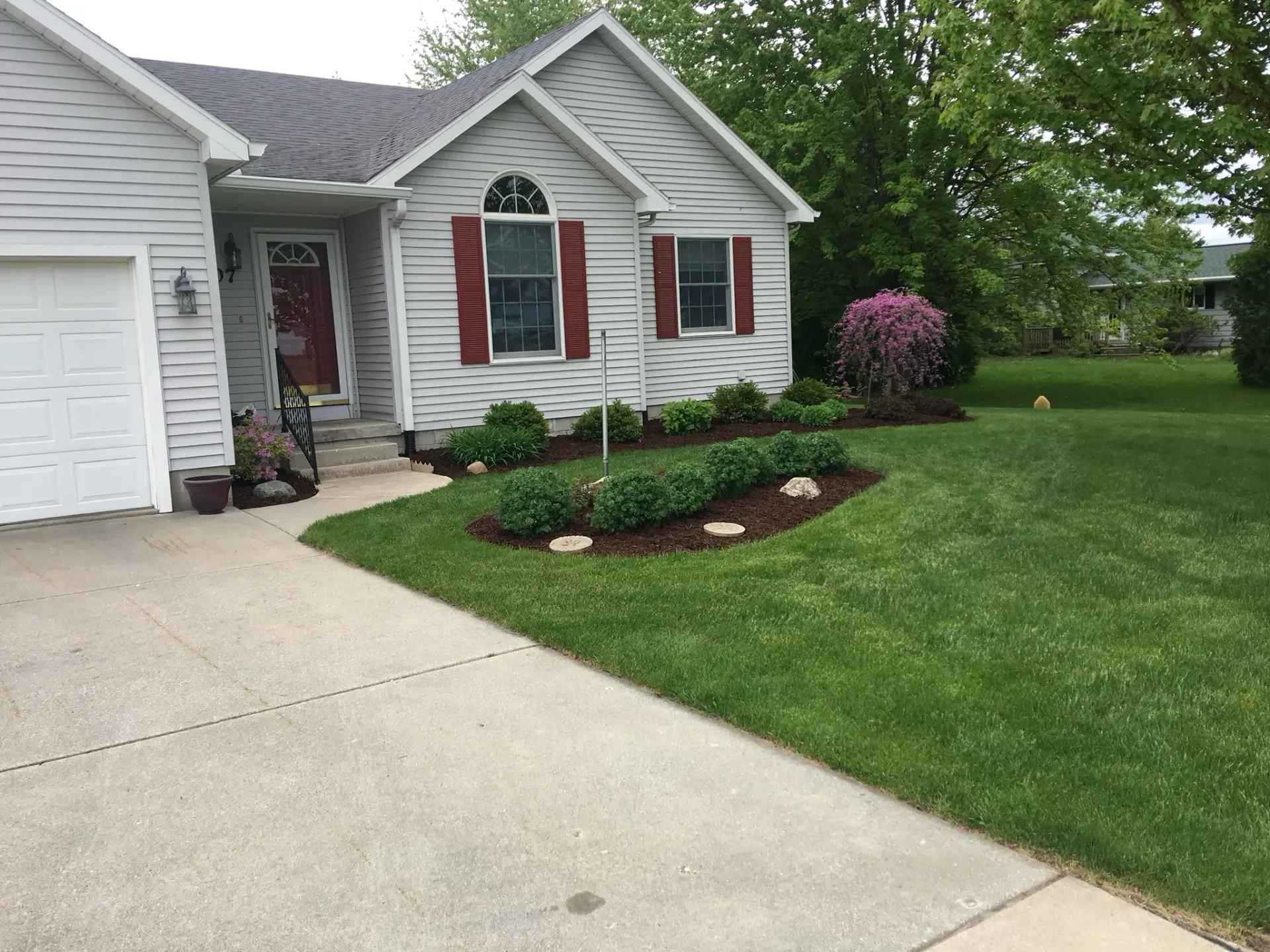 House with gray siding, red shutters, and a well-manicured lawn and flowerbed.