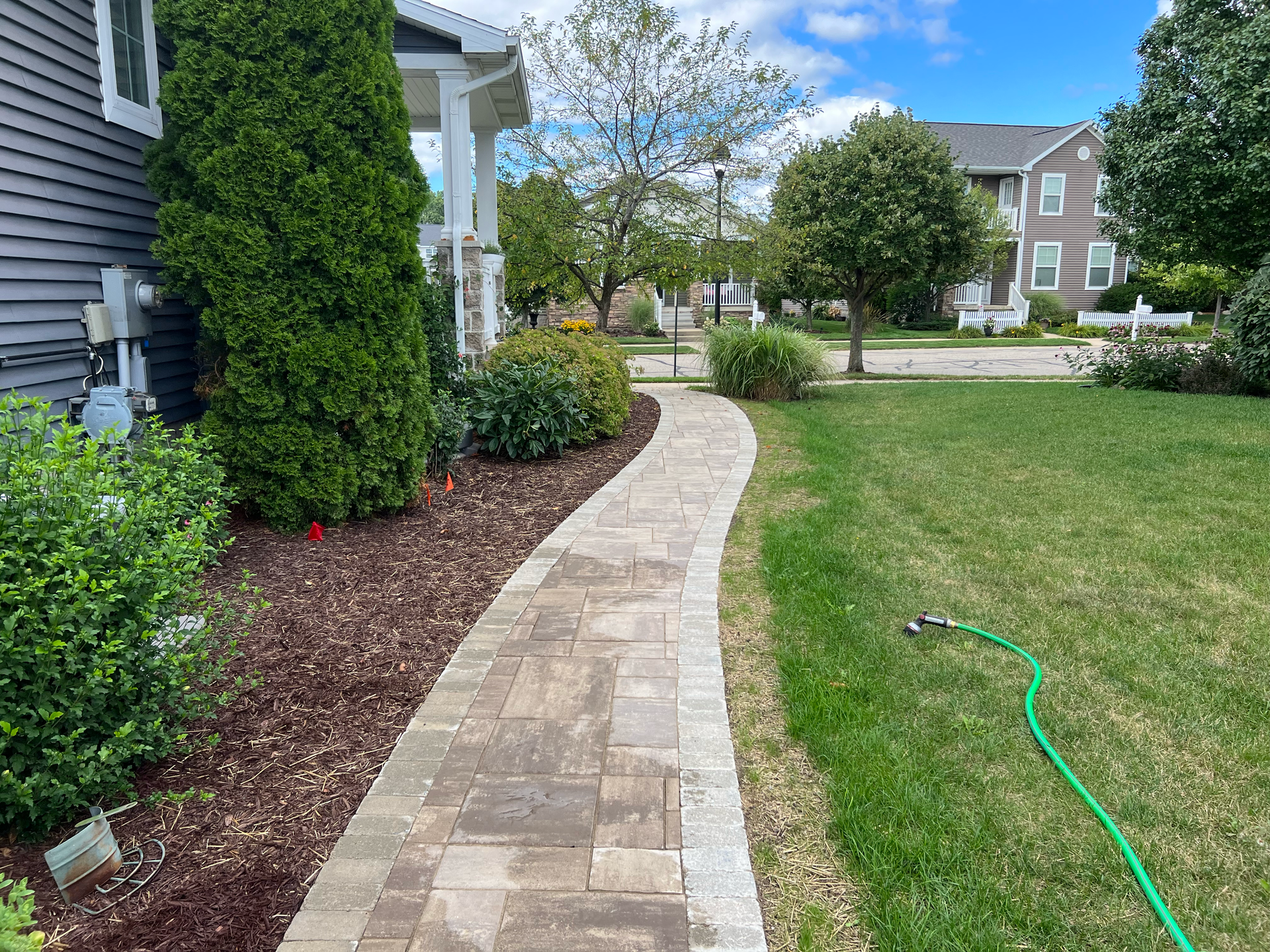 Brick pathway leading to a house with a green lawn and landscaping.