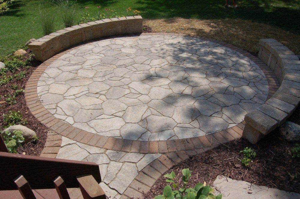 Circular stone patio with curved seating, surrounded by landscaping and grass.