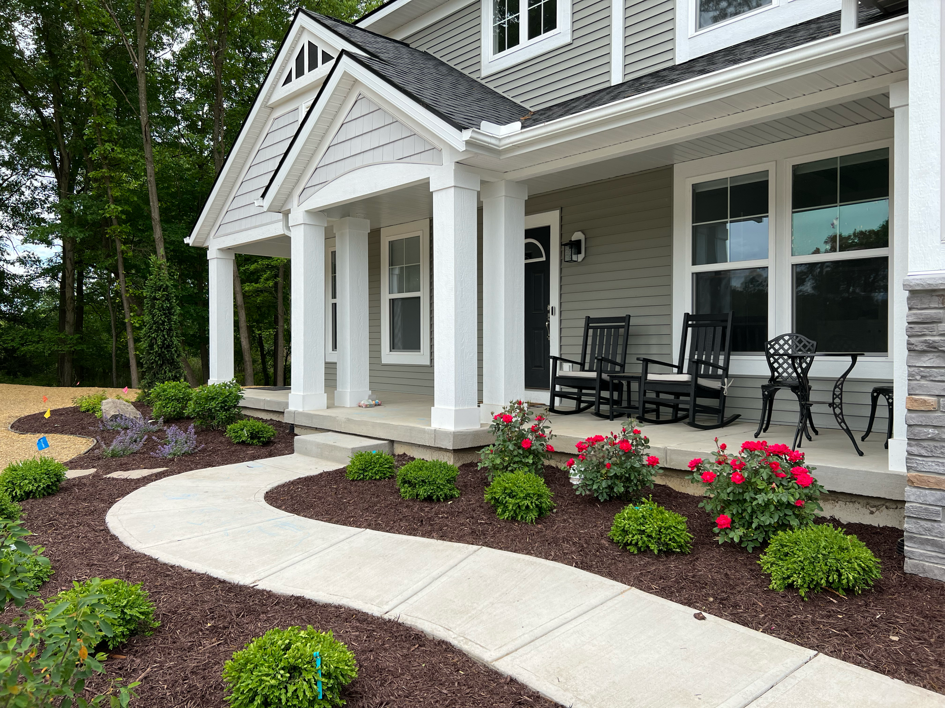 Curving walkway to a house with a porch and landscaping, green siding, and pink rose bushes.