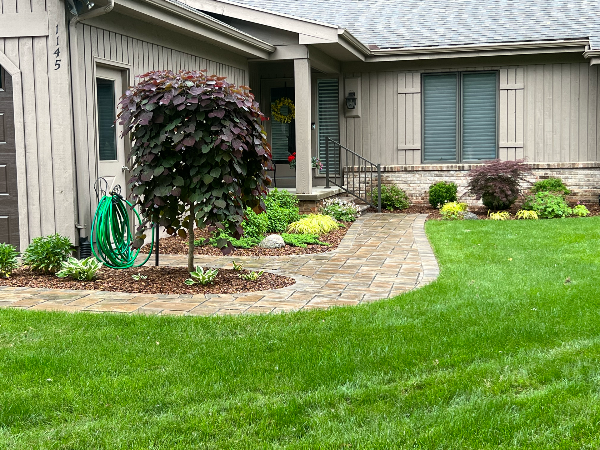 A brick pathway leads to a house with well-kept landscaping and a green lawn.