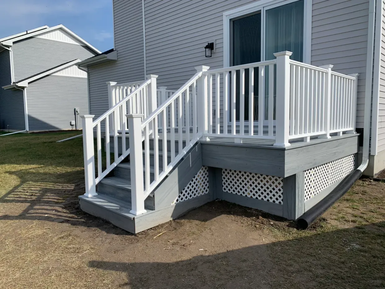 White deck with gray base and railing, steps leading up to a sliding door on a sunny day.