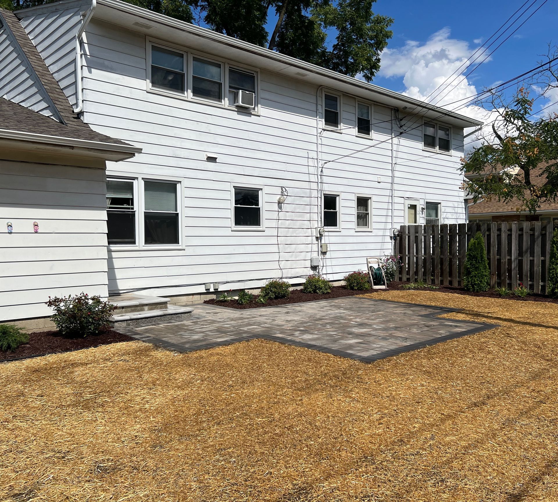 Backyard with a two-story white house, patio, gravel, and a wooden fence.