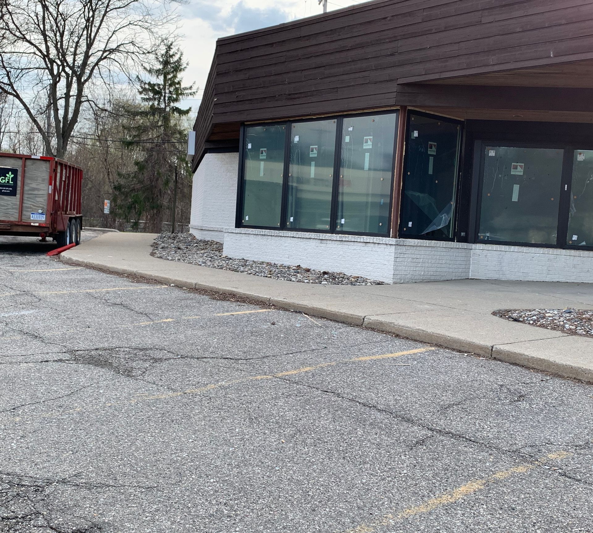 Exterior view of a building with large windows, a parking lot, and a dumpster.