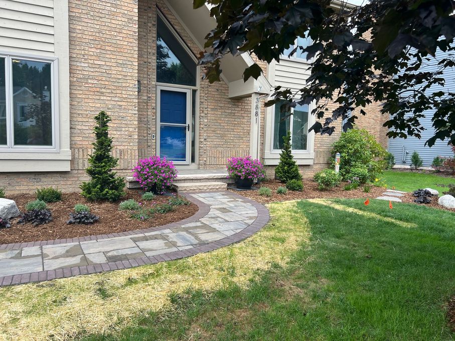 Stone walkway leading to a brick house with landscaping, lush lawn, and blooming pink flowers.