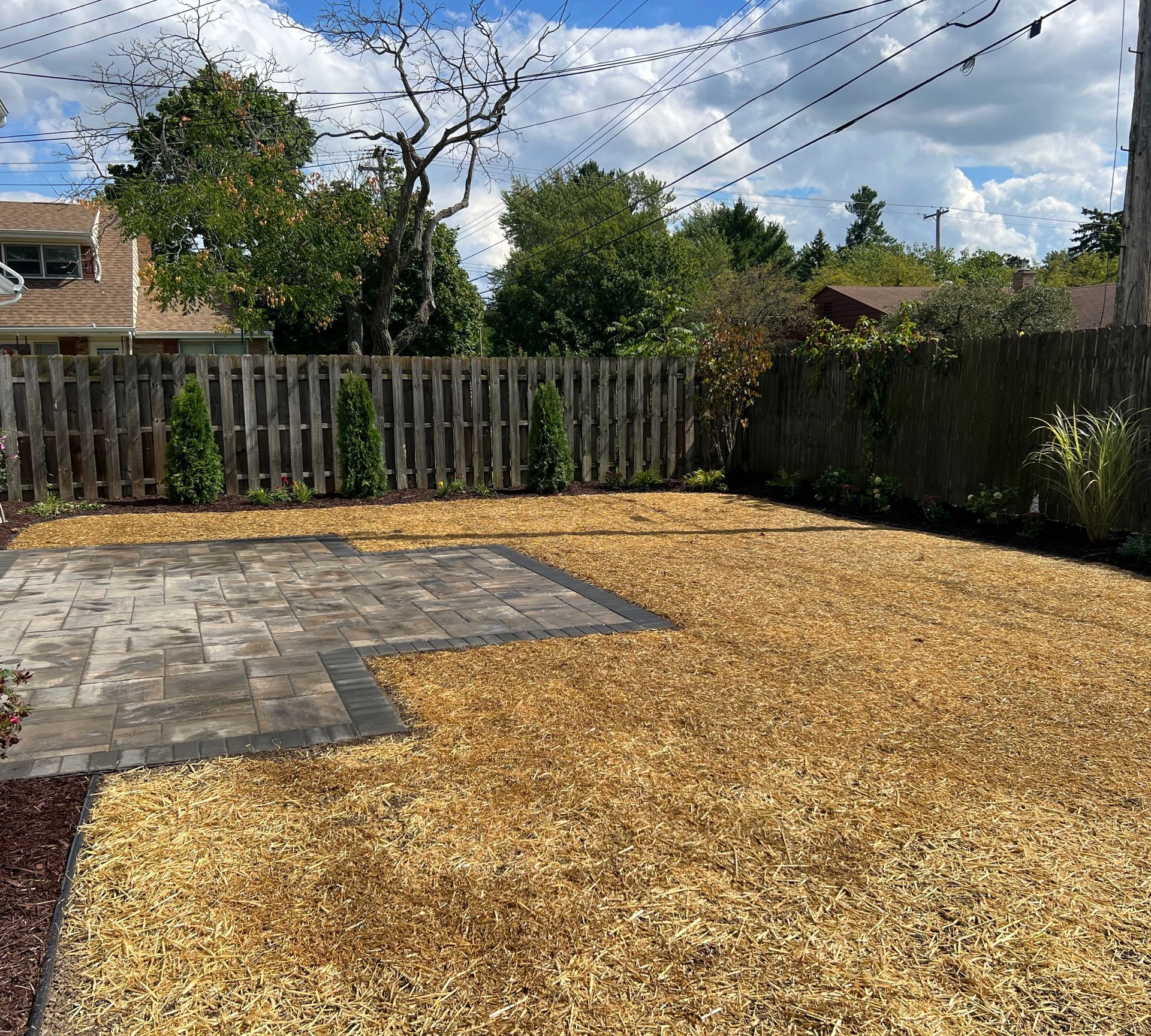 Backyard with wood chip ground cover, patio, and wooden fence.