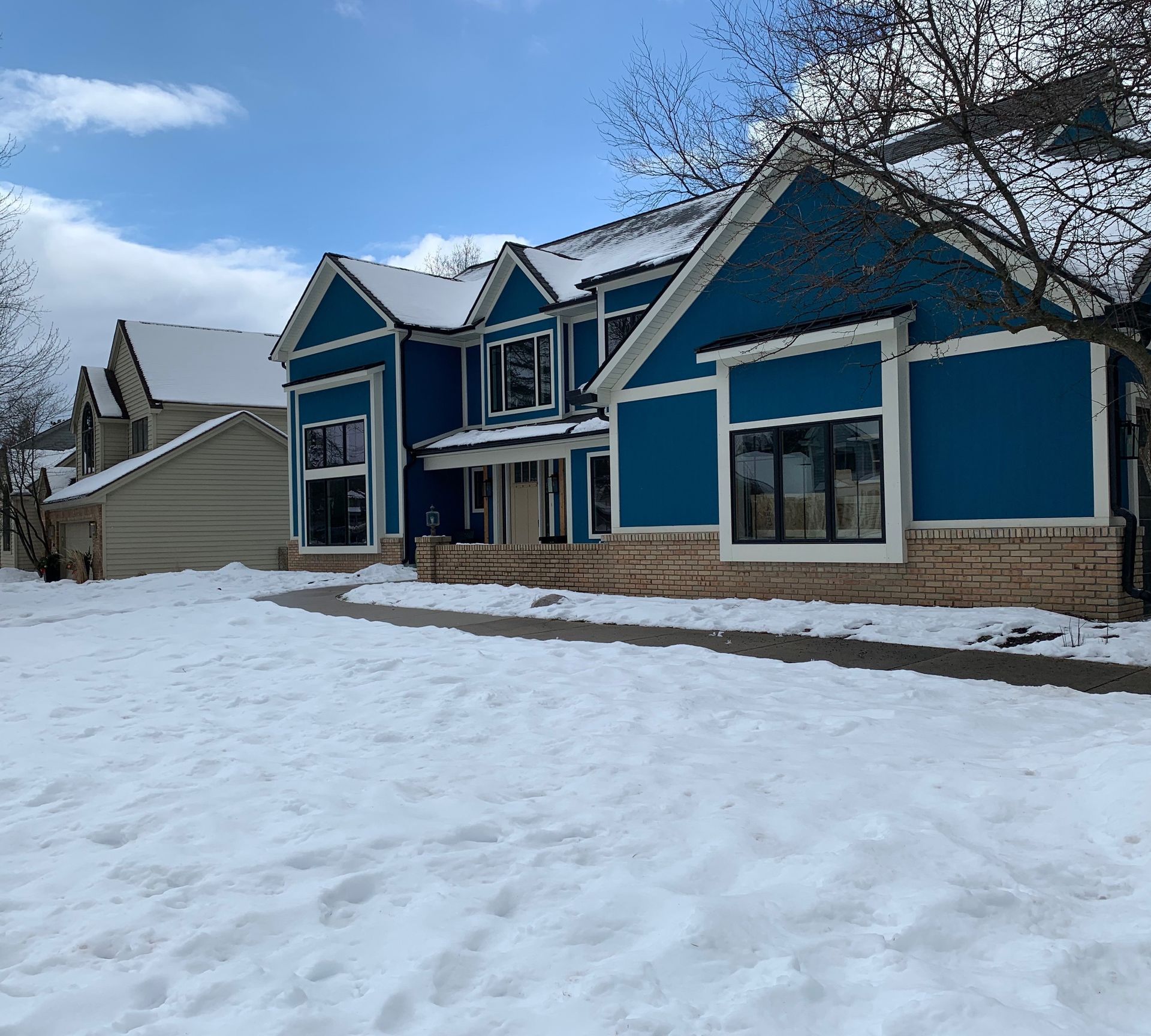 Blue house with snow-covered yard under a partly cloudy sky.