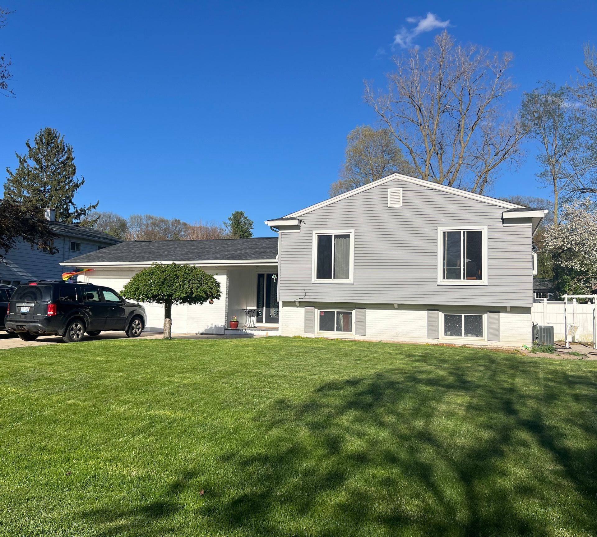 Gray-sided house with black car in driveway, on a green lawn under a blue sky.