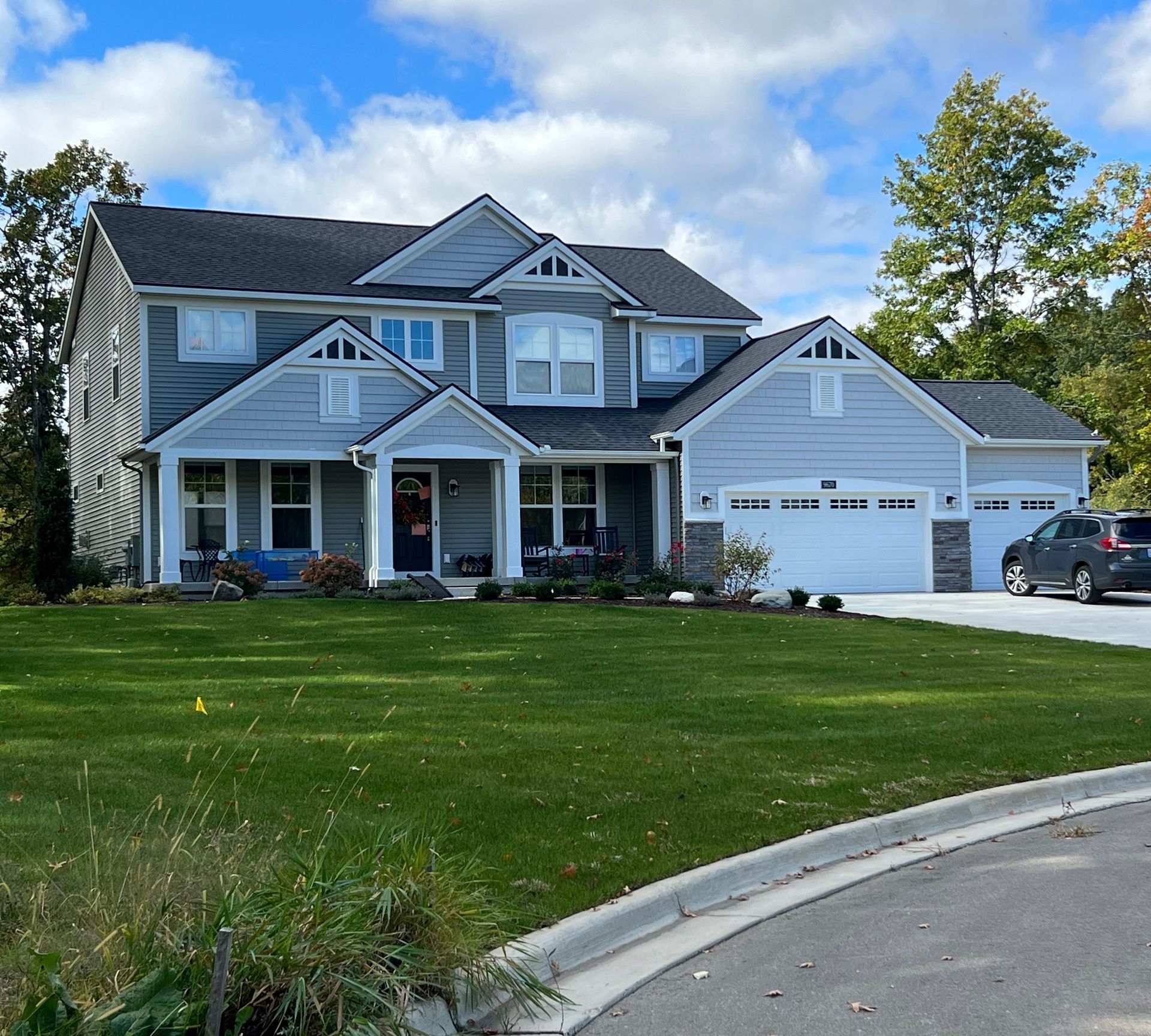 Two-story gray house with white trim, lawn, and a driveway. Blue sky with trees.