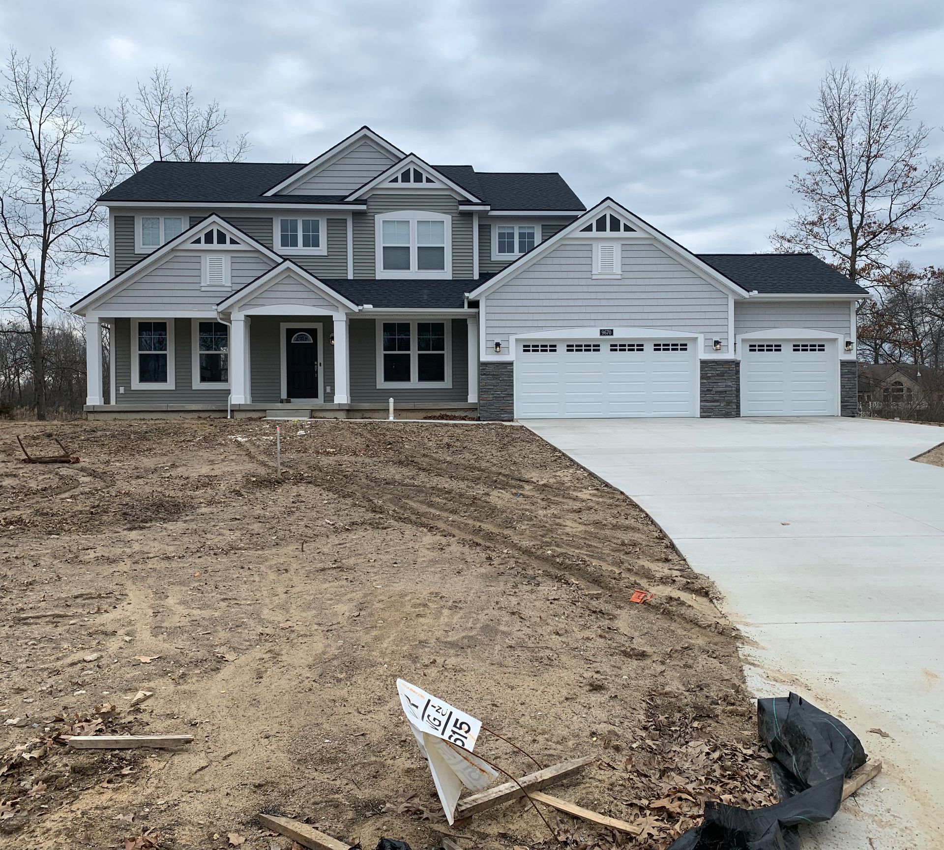 New two-story house with gray siding, white garage doors, and a concrete driveway, under a cloudy sky.