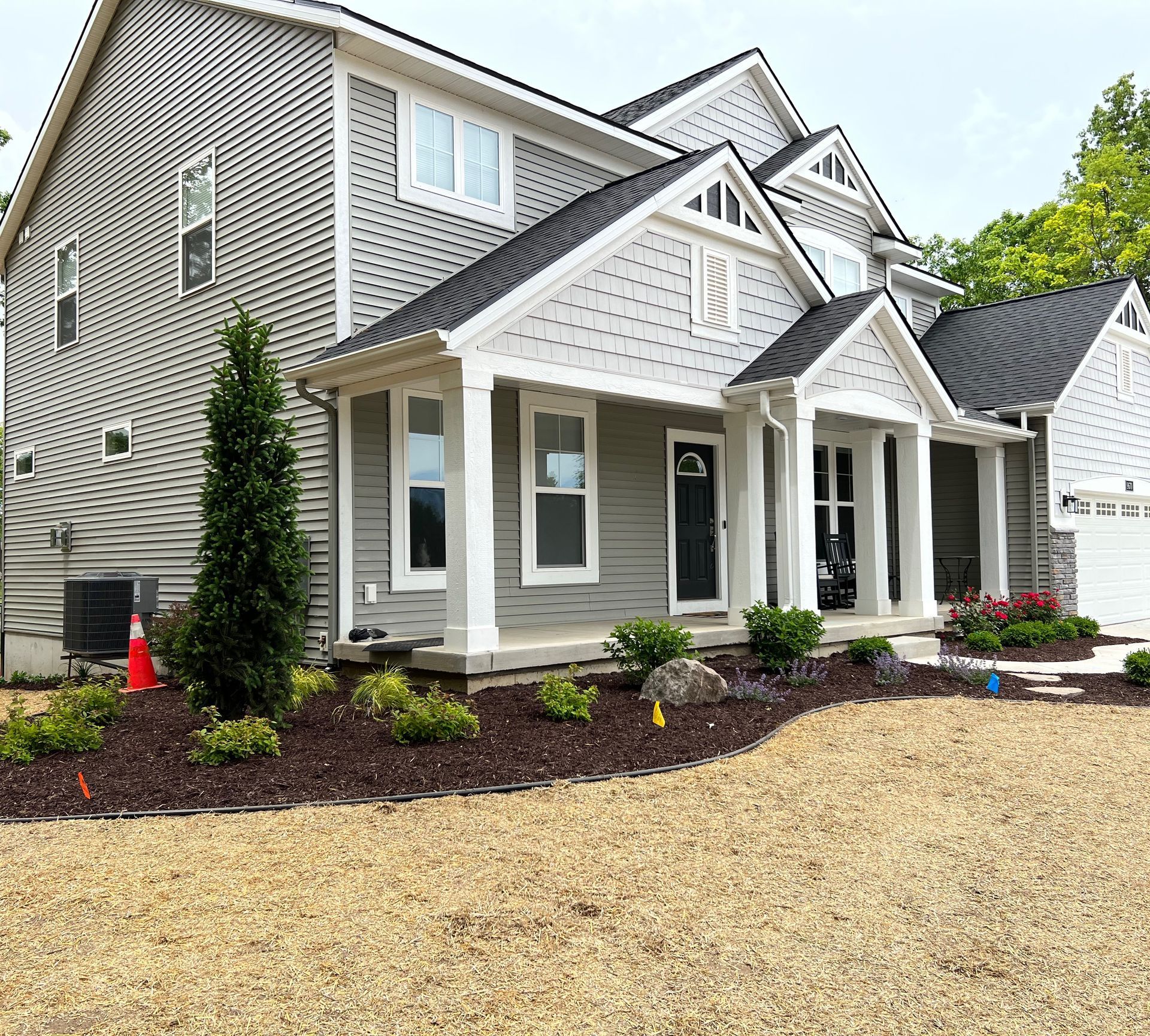 Gray two-story house with white trim, black door, and dark roof; small landscaping in front.