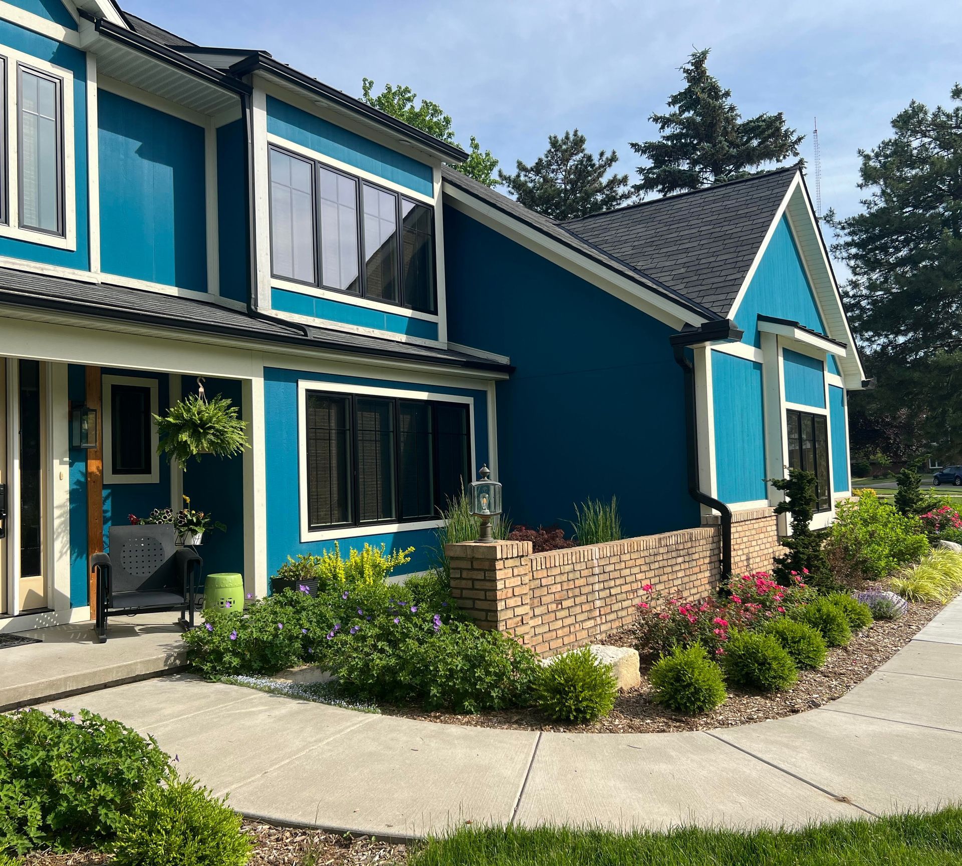 Two-story teal house with black trim, surrounded by landscaping, including a brick wall and a concrete walkway.