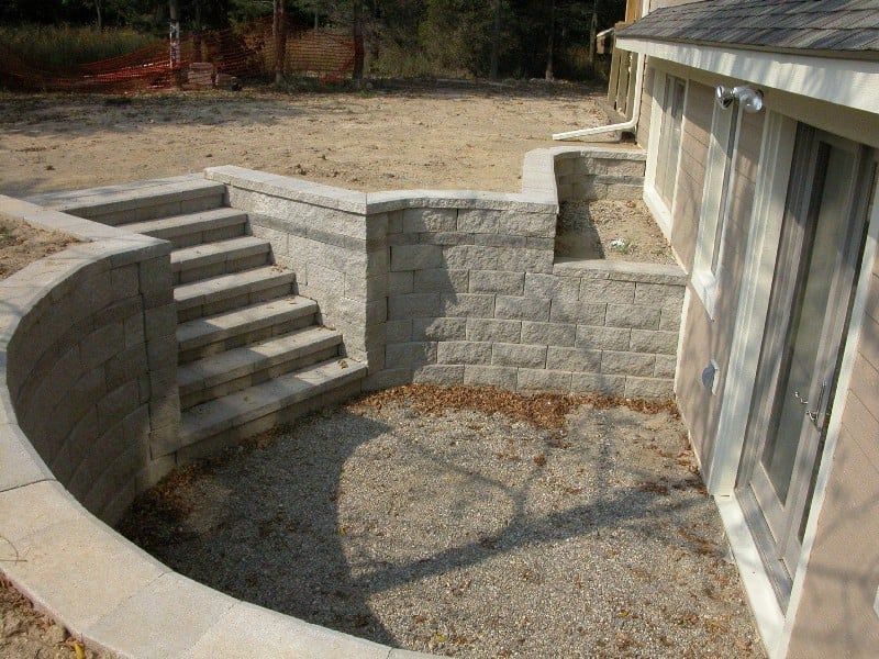 Stone retaining walls with stairs leading down to a basement walkout. Gravel ground.