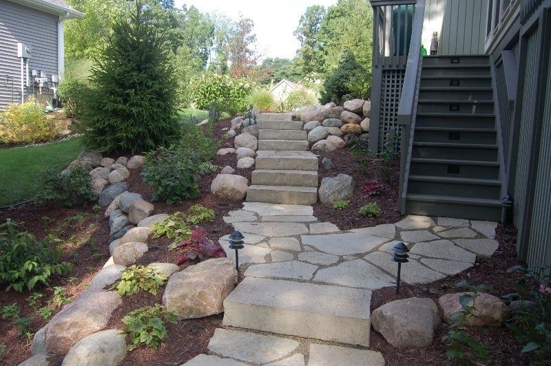 Stone steps lead up a landscaped hillside, flanked by rocks and greenery.