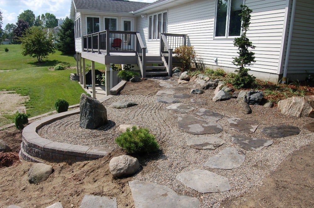 Backyard with stone path, deck, and landscaping with rocks and plants.
