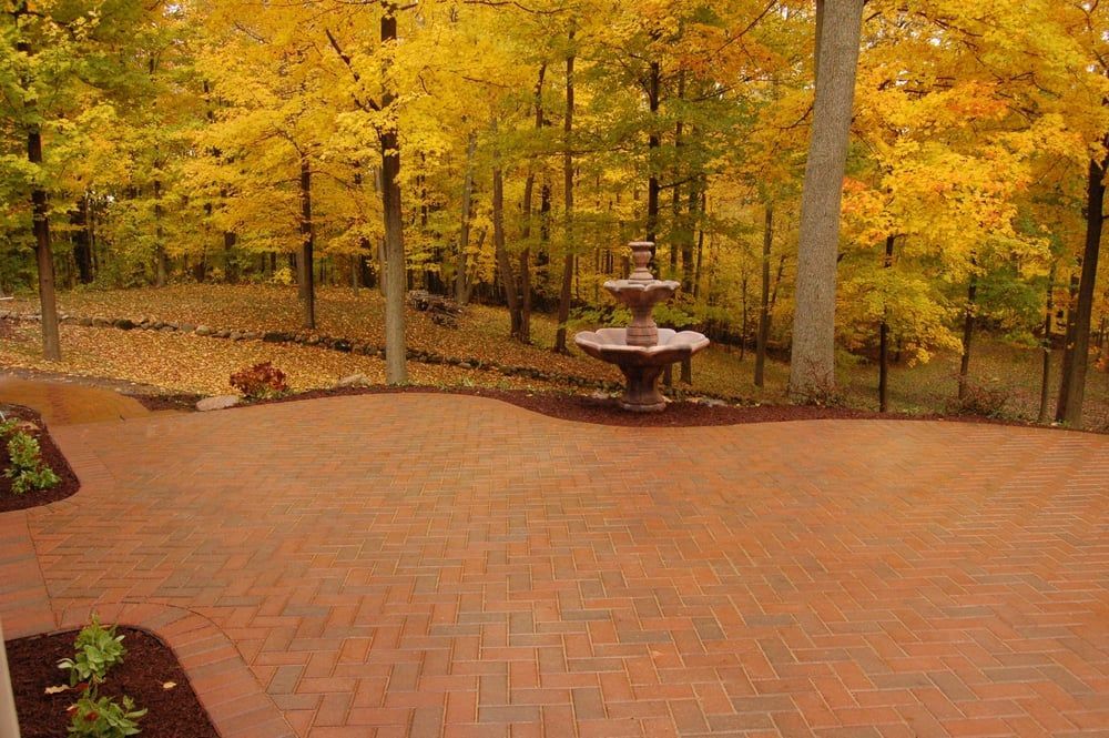 Brick patio with fountain, surrounded by autumn trees with yellow foliage.