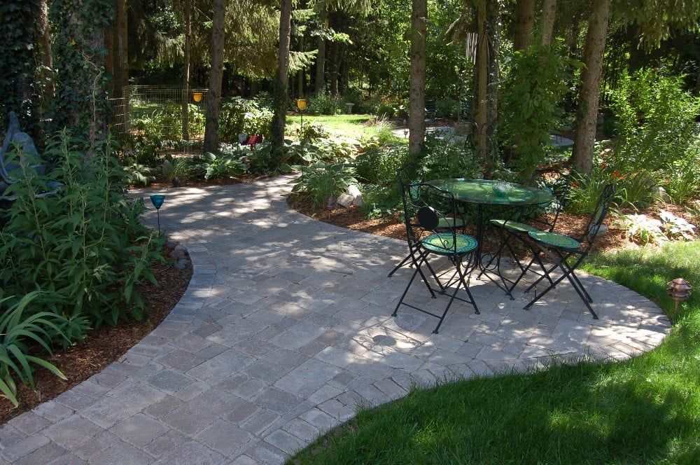 Brick patio with small table and chairs in a garden setting, surrounded by trees and greenery.