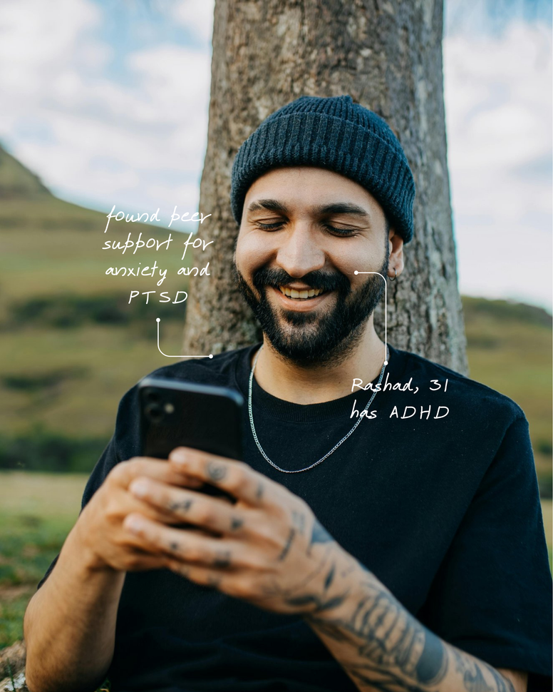 A man with a beard is smiling while looking at his phone.