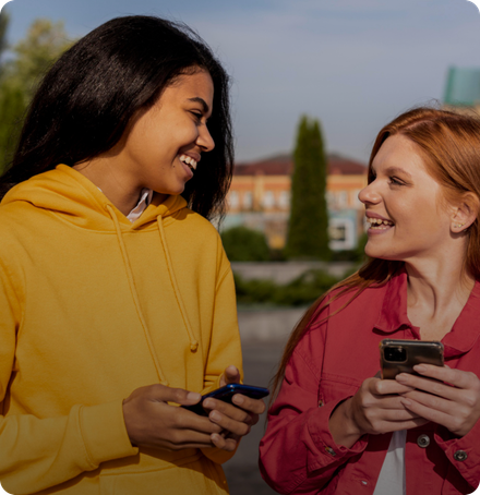 Two women are laughing and looking at their cell phones.