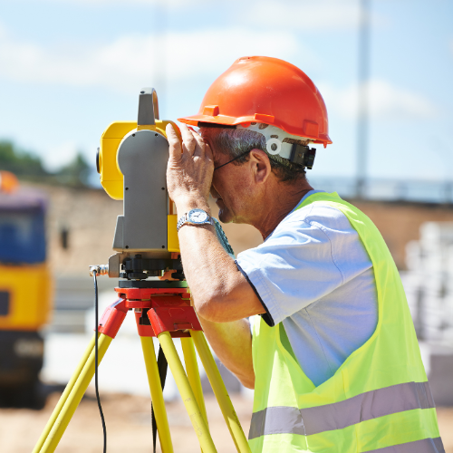 A man wearing a hard hat and safety vest is looking through a telescope