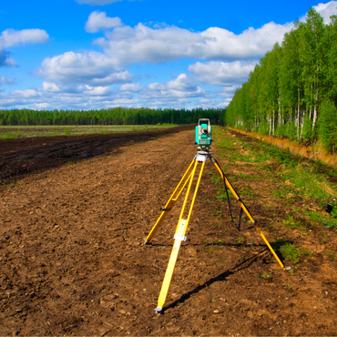 A total station is sitting in the middle of a dirt field.