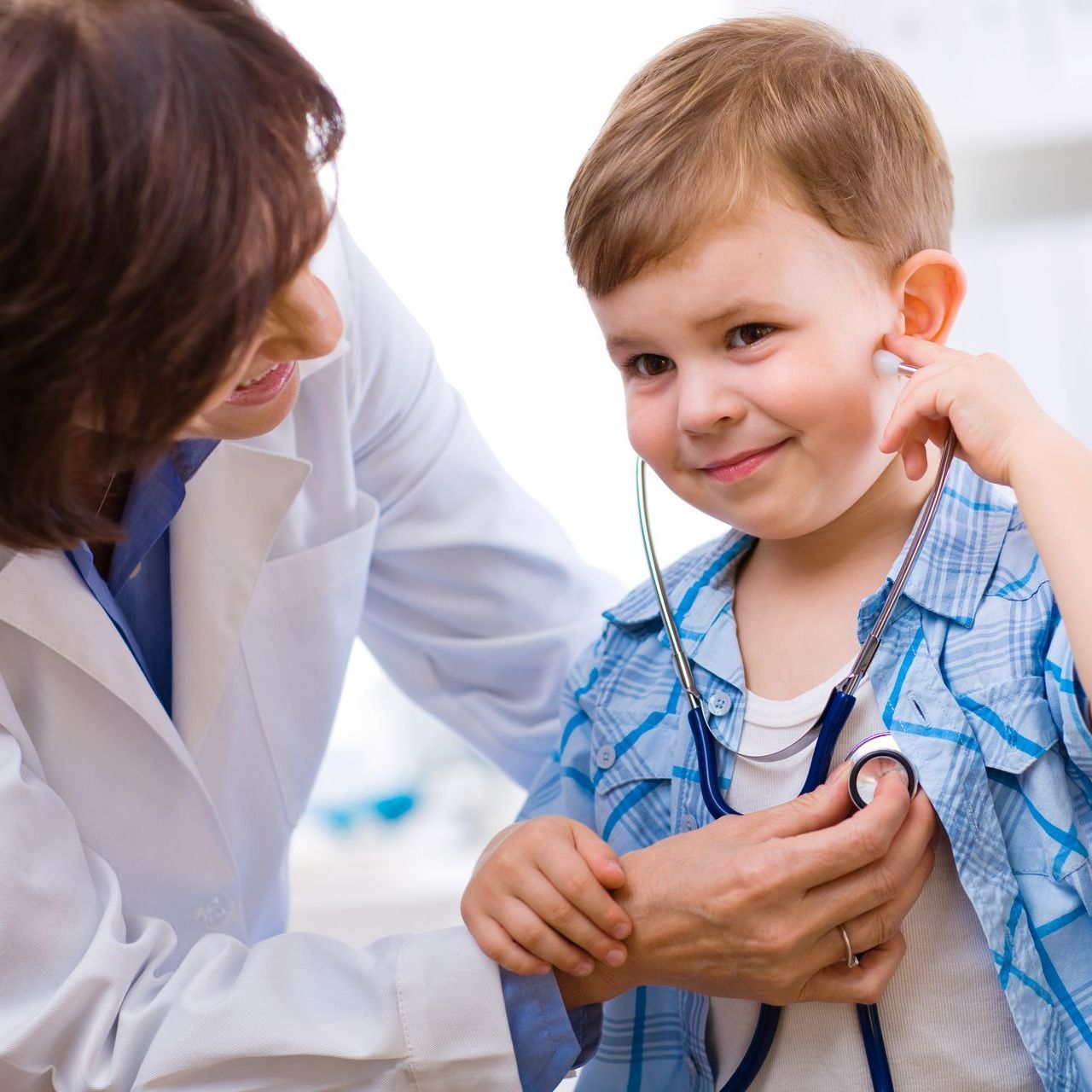 Female doctor checking young boy's heart with a stethoscope.