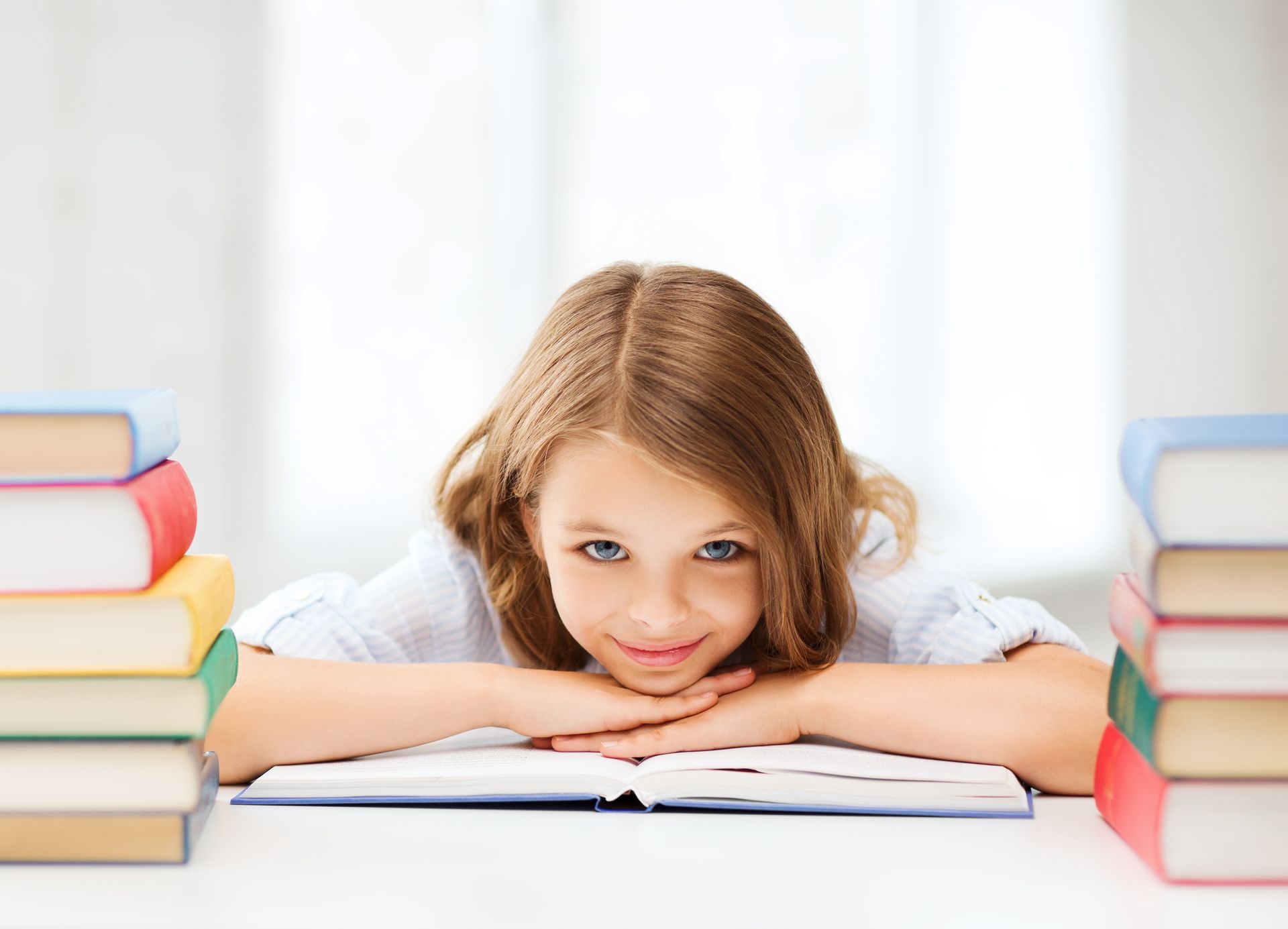 A little girl is sitting at a table with a stack of books.