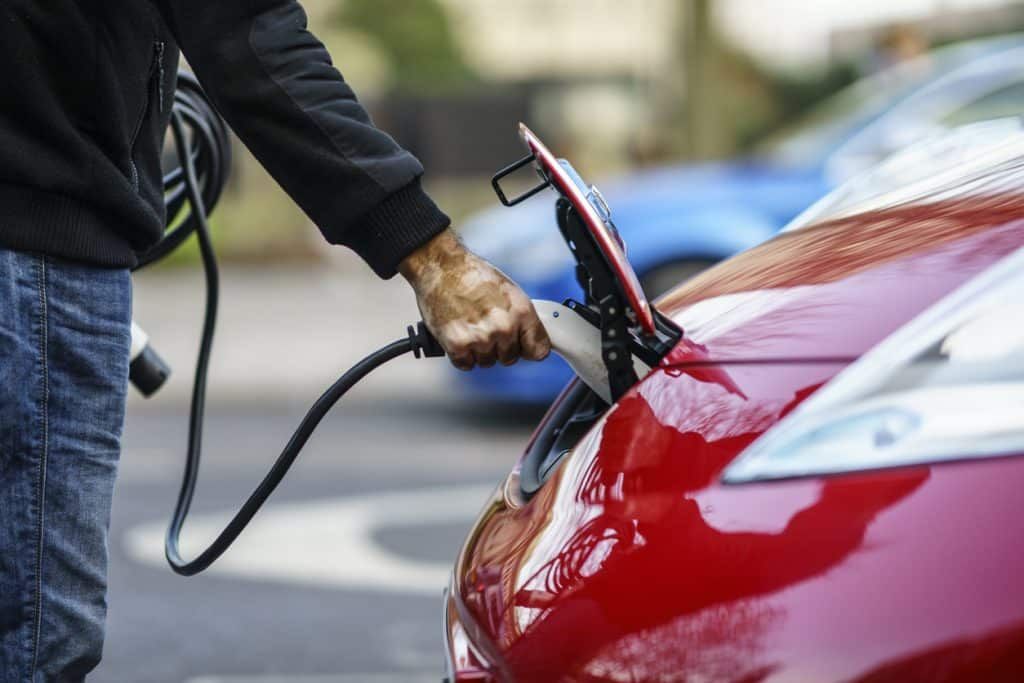 A man is charging an electric car in a parking lot.