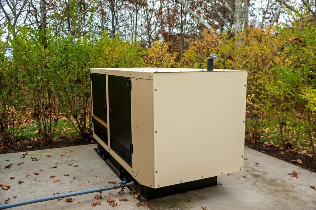A generator is sitting on a concrete surface in the woods.