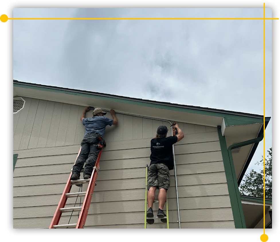 Two men are working on the side of a house on a ladder.