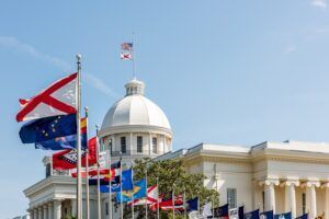 A row of flags are flying in front of a large building.