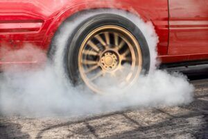 Smoke is coming out of the tire of a red car.