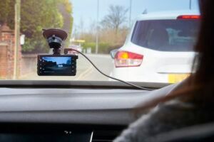 A woman is driving a car with a dash cam attached to the windshield.