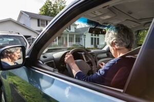 An elderly woman is driving a car on a country road.