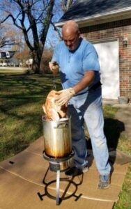 A man is cooking a turkey in a pot outside of a house.
