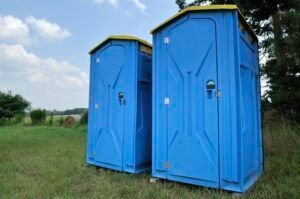 Two blue portable toilets are sitting in a grassy field.