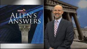 A man in a suit and tie is standing in front of a sign that says allen 's answers