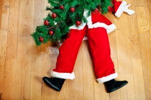 A person dressed as santa claus is laying on the floor holding a christmas tree.
