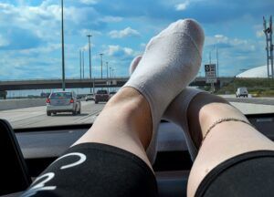 A person wearing white socks is sitting in the driver 's seat of a car.