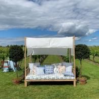 Outdoor white canopy daybed on a grassy lawn, with patterned pillows under a cloudy sky.