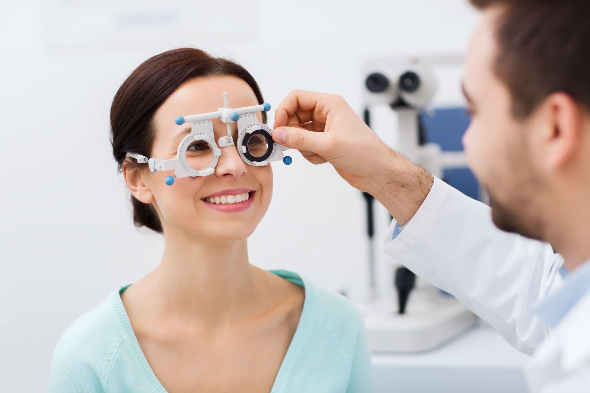 Eye exam with phoropter as an optometrist adjusts lenses for a smiling patient Eye exam with phoropter as an optometrist adjusts lenses for a smiling patient