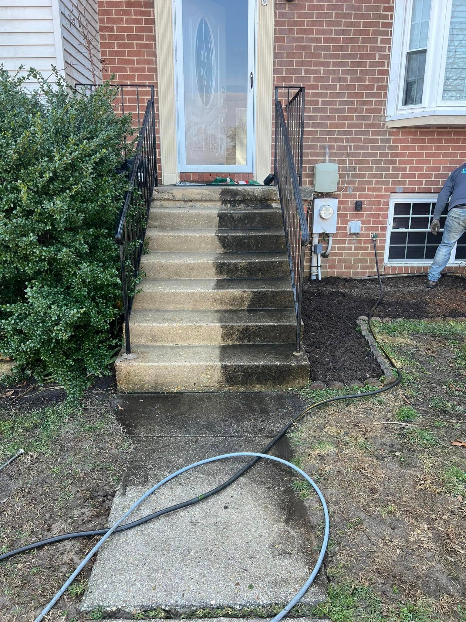 Front steps to a brick house with a glass door, wet concrete path, and a hose lying across the walkway.