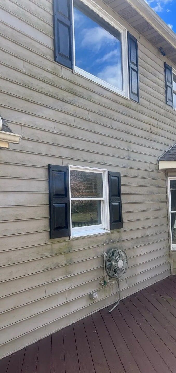 Exterior of a beige house with blue shutters, a window, wall-mounted fan, and brown deck below