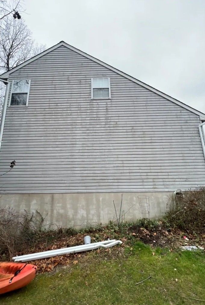 Gray-sided house exterior with a concrete foundation and yard debris in the foreground