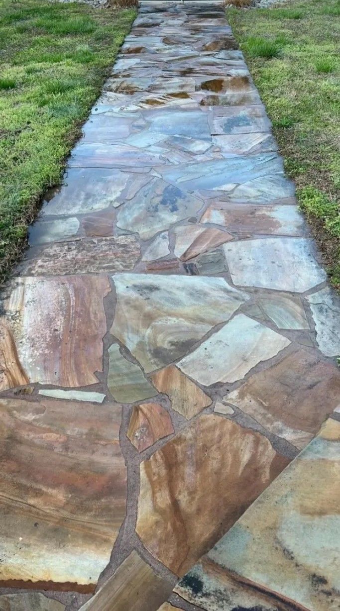 Stone walkway path set in grass, made of multicolored irregular slabs.
