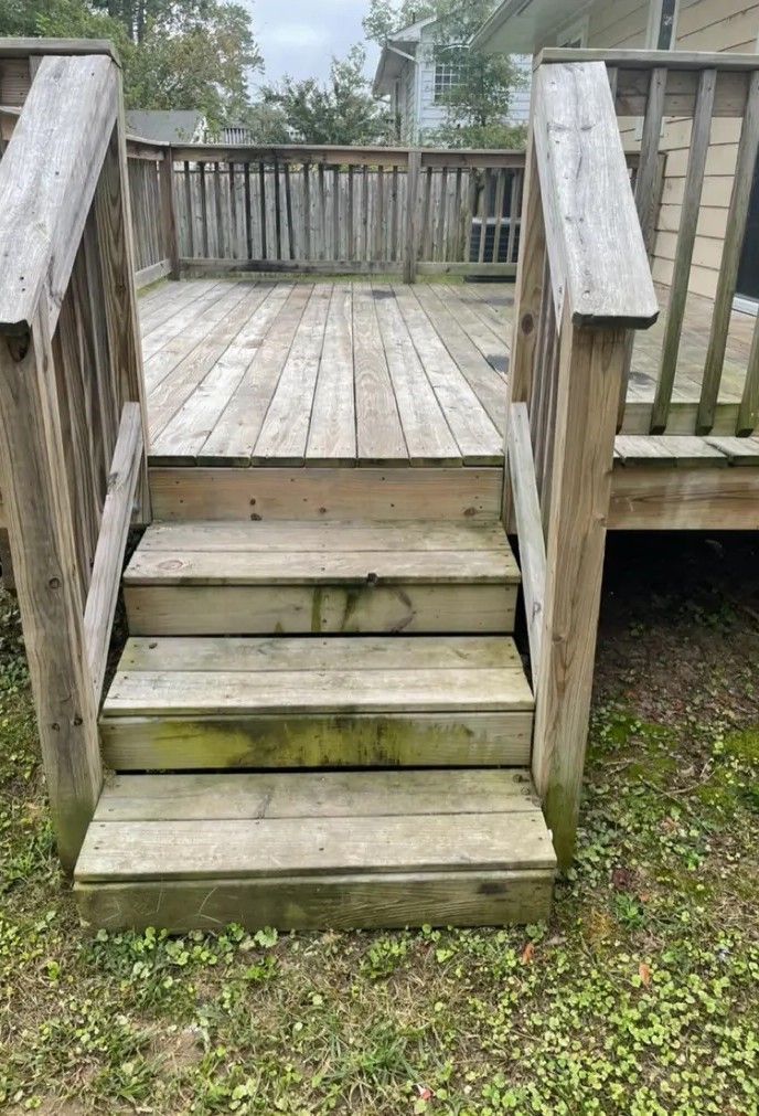 Weathered wooden deck stairs leading to a small porch in a backyard.