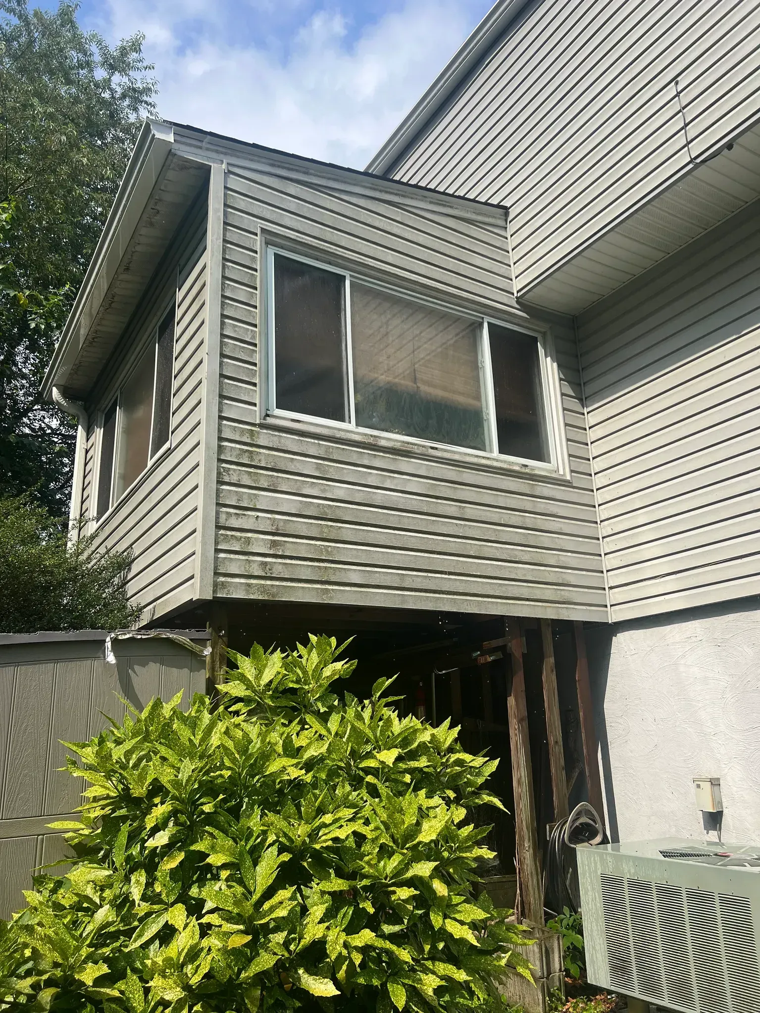 Exterior view of a gray house with a bay window, sloped roof, and shrubs in the foreground