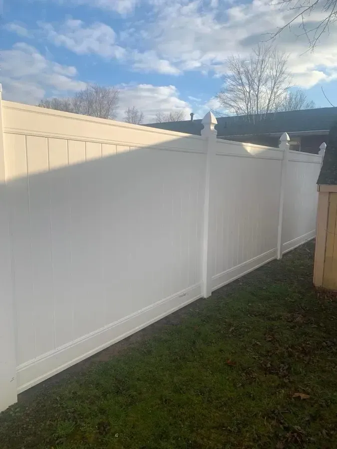 White vinyl fence along a grassy yard under a partly cloudy sky.